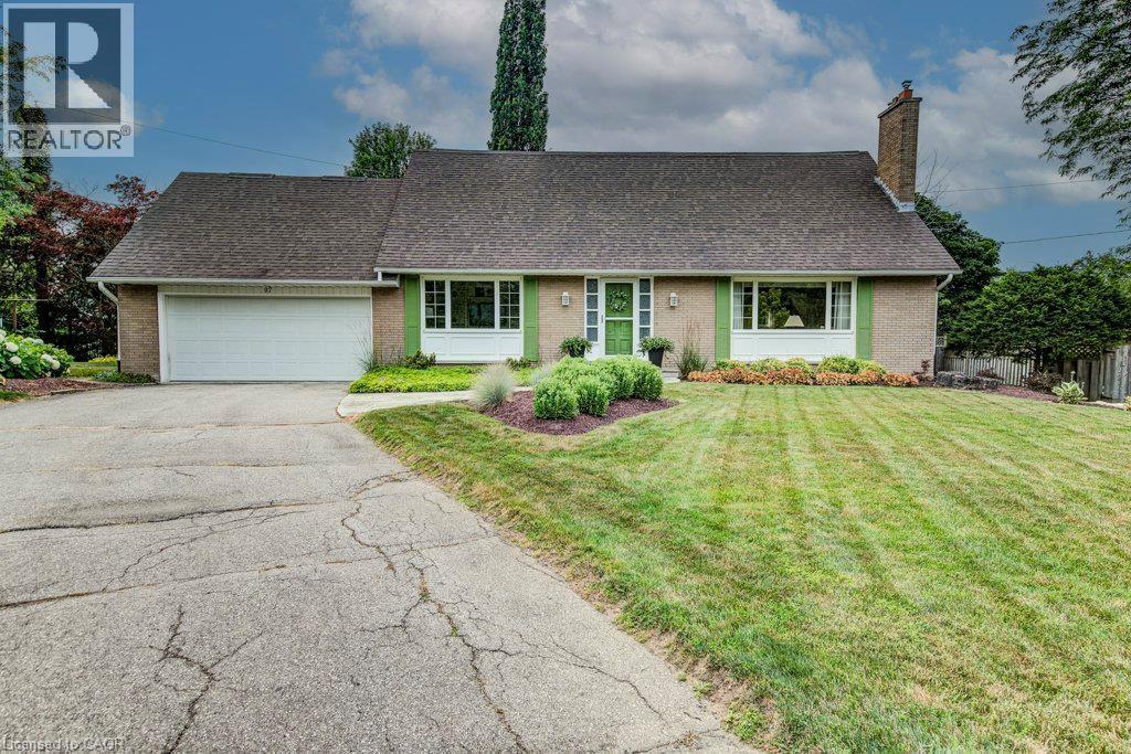Brick facade residence featuring a two-car garage, mature landscaping, a central green entry door, and decorative green window shutters - 97 Somerset Crescent, Waterloo, ON - Outdoor