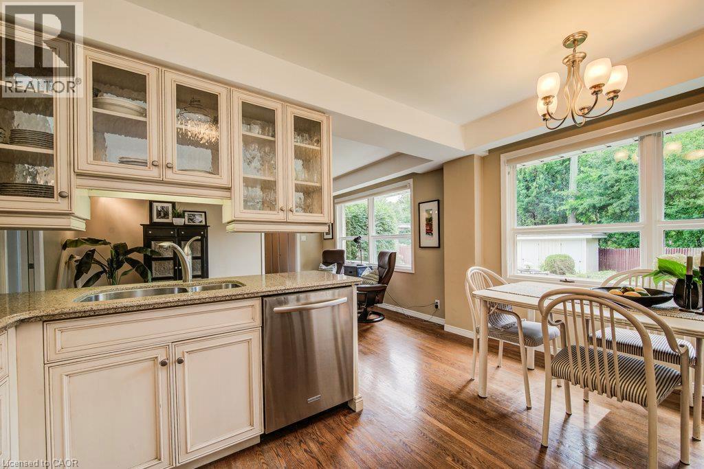 Kitchen and dining area featuring wood-finish flooring, built-in cabinetry with glass inserts, stainless steel dishwasher, a double basin sink, and a multi-light chandelier - 97 Somerset Crescent, Waterloo, ON - Indoor