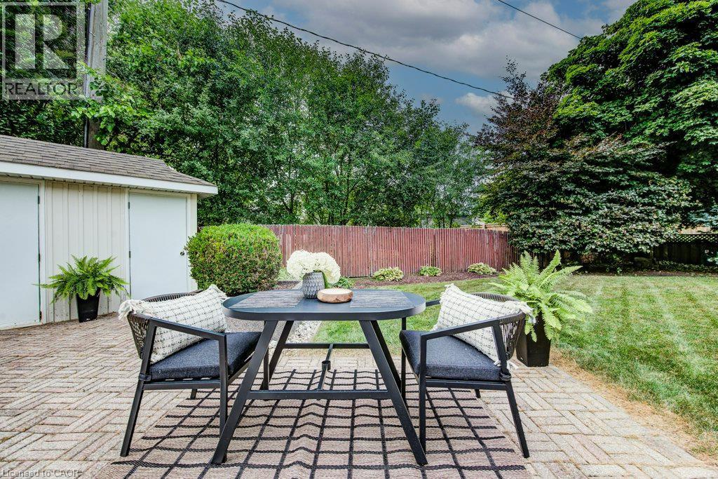 Expansive backyard patio featuring brick paver flooring, a detached shed with double doors, a manicured lawn, and mature perimeter trees - 97 Somerset Crescent, Waterloo, ON - Outdoor With Deck Patio Veranda