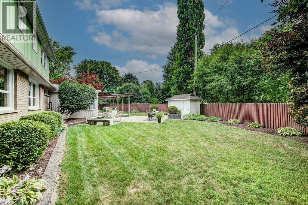Spacious backyard featuring a manicured lawn, stone patio with pergola, privacy fencing, mature landscaping, and an outdoor storage shed - 97 Somerset Crescent, Waterloo, ON - Outdoor
