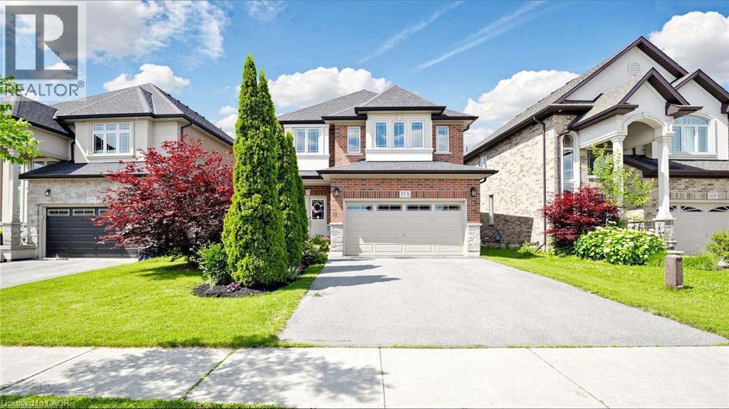 Brick facade with stone accents, two-car garage, concrete driveway, front lawn, and established landscaping - 173 Raymond Road, Ancaster, ON - Outdoor With Facade