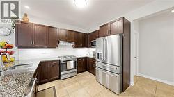 Kitchen featuring wood-finish cabinetry, granite-style countertops, stainless steel appliances, a tile backsplash, and tile flooring -