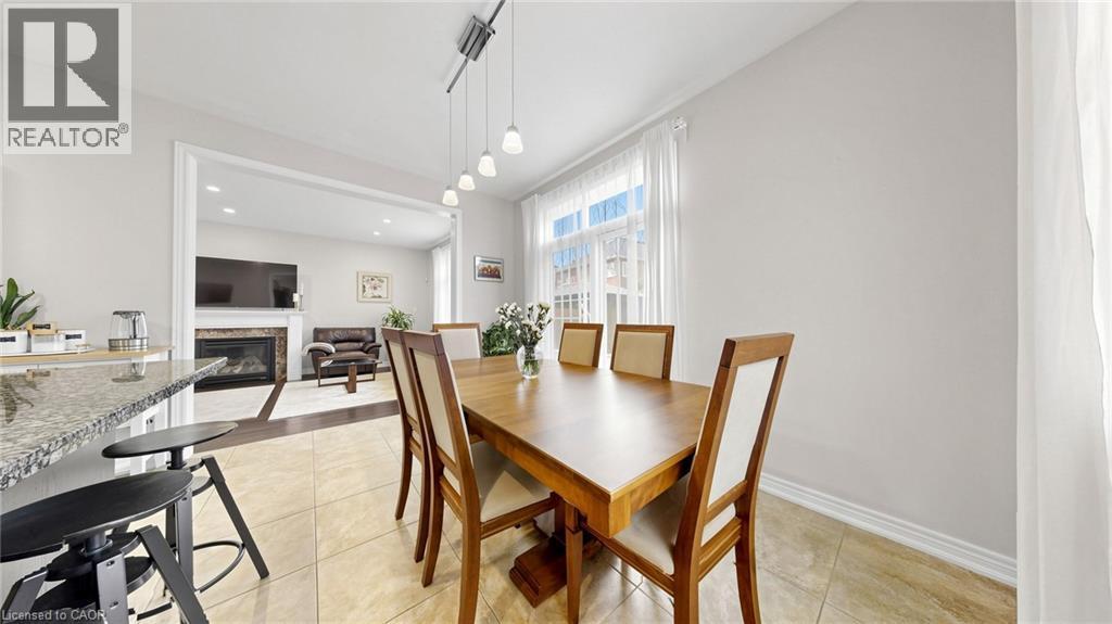Dining area with tile flooring and track lighting, featuring a window with natural light and an open doorway to a living space with a fireplace - 173 Raymond Road, Ancaster, ON - Indoor Photo Showing Dining Room