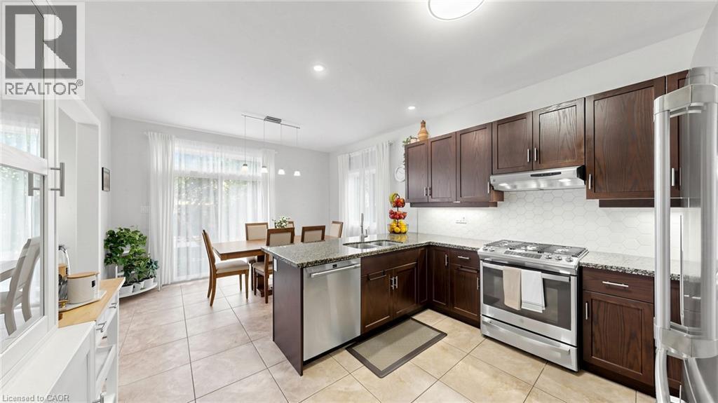 Kitchen featuring dark wood cabinetry, stainless steel appliances, light-toned hexagon tile backsplash, and light-toned granite countertops - 173 Raymond Road, Ancaster, ON - Indoor Photo Showing Kitchen With Stainless Steel Kitchen With Double Sink
