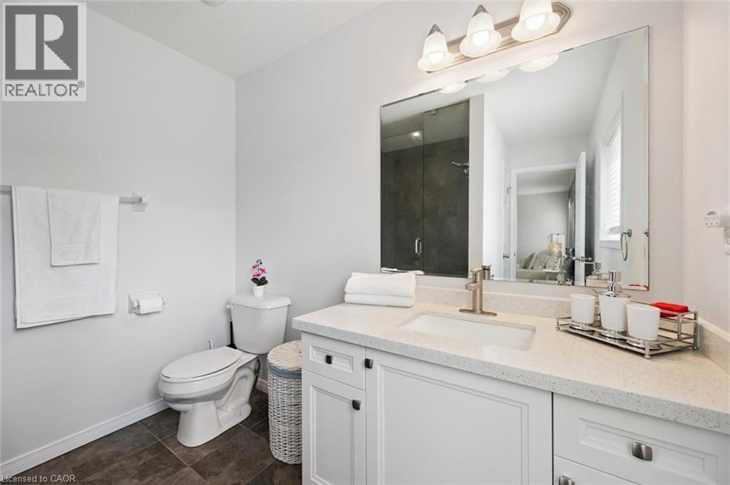 Bathroom featuring a single vanity with an integrated sink, light-colored countertop, white cabinetry, dark tile flooring, and a glass-enclosed shower - 360 Freure Drive, Cambridge, ON - Indoor Photo Showing Bathroom