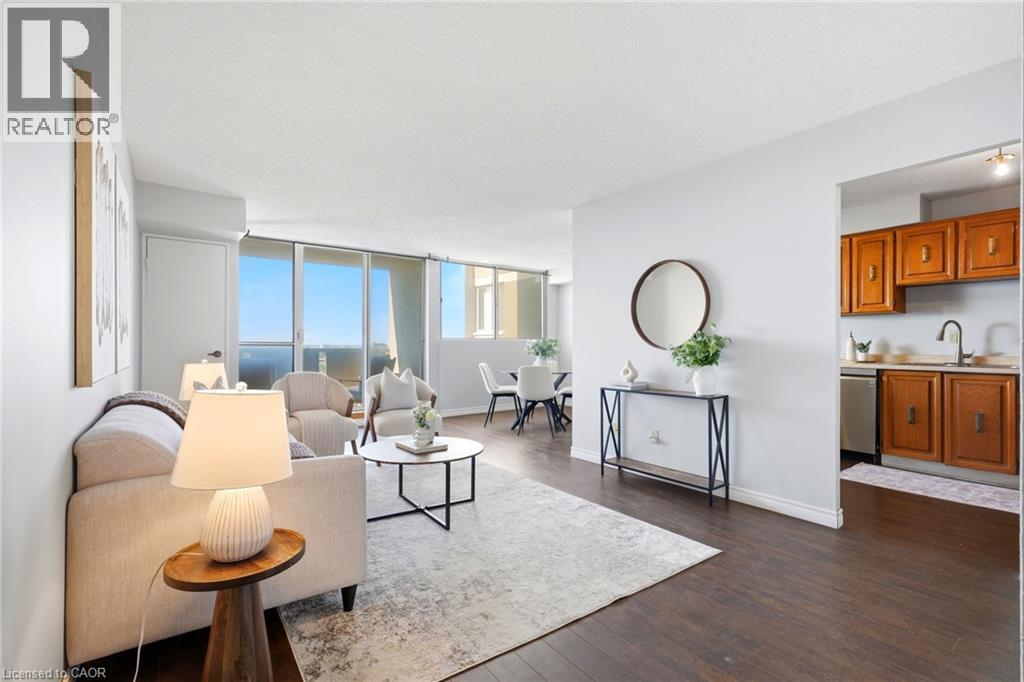 Dark wood-finish flooring throughout, bright white walls, and a kitchen featuring wood cabinetry and a stainless-steel dishwasher - 375 King Street N Unit# 708, Waterloo, ON - Indoor