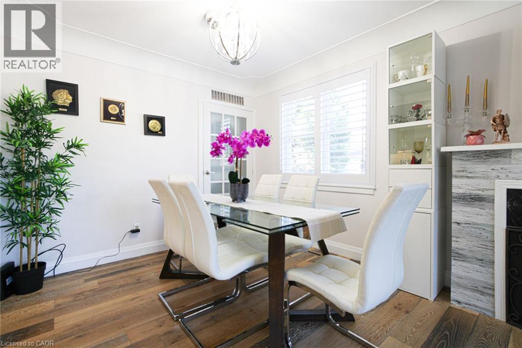 Wood-finish flooring, white wall paint, window with white louvered shutters, glass-front display cabinetry, and a decorative fireplace surround - 2105 Maplewood Drive, Burlington, ON - Indoor Photo Showing Dining Room