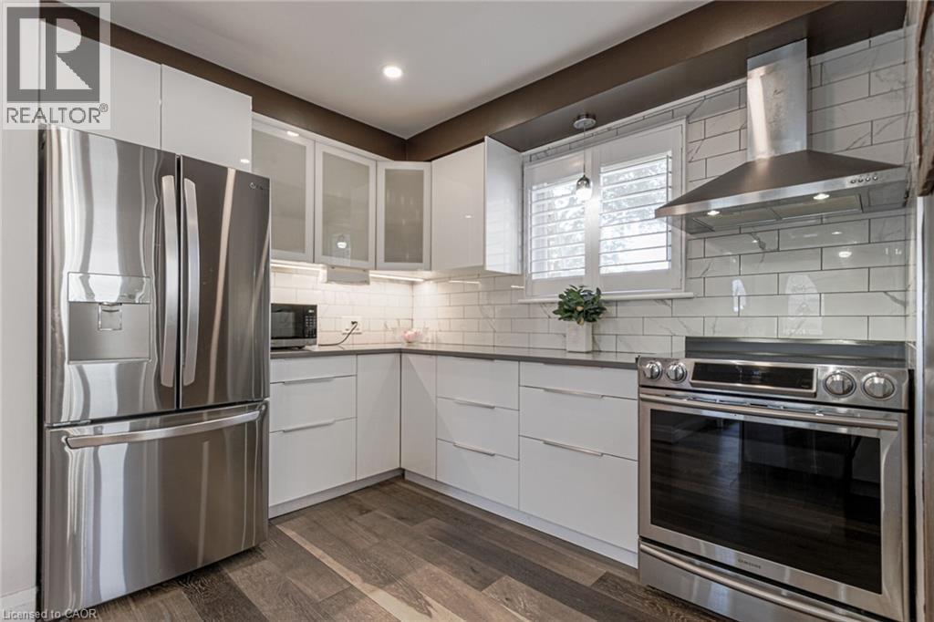 Sleek kitchen featuring stainless steel appliances, white flat-panel cabinetry, dark countertops, and wood-finish flooring - 2105 Maplewood Drive, Burlington, ON - Indoor Photo Showing Kitchen With Stainless Steel Kitchen