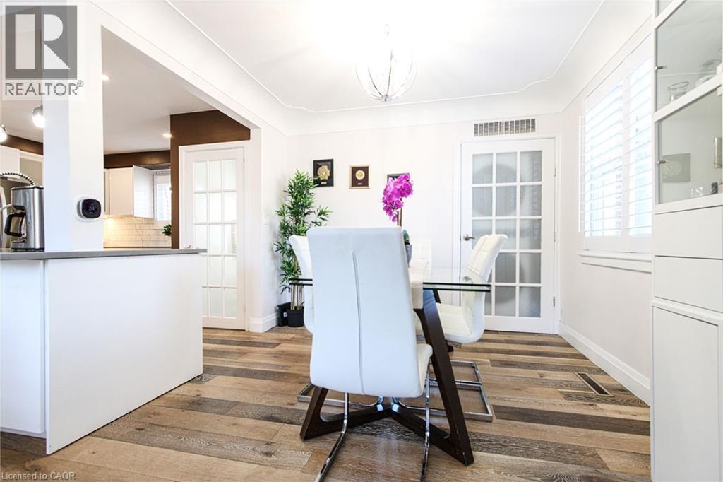 Wood-finish flooring throughout, white plantation shutters, white built-in cabinetry with glass fronts, and a white paneled door with glass inserts - 2105 Maplewood Drive, Burlington, ON - Indoor