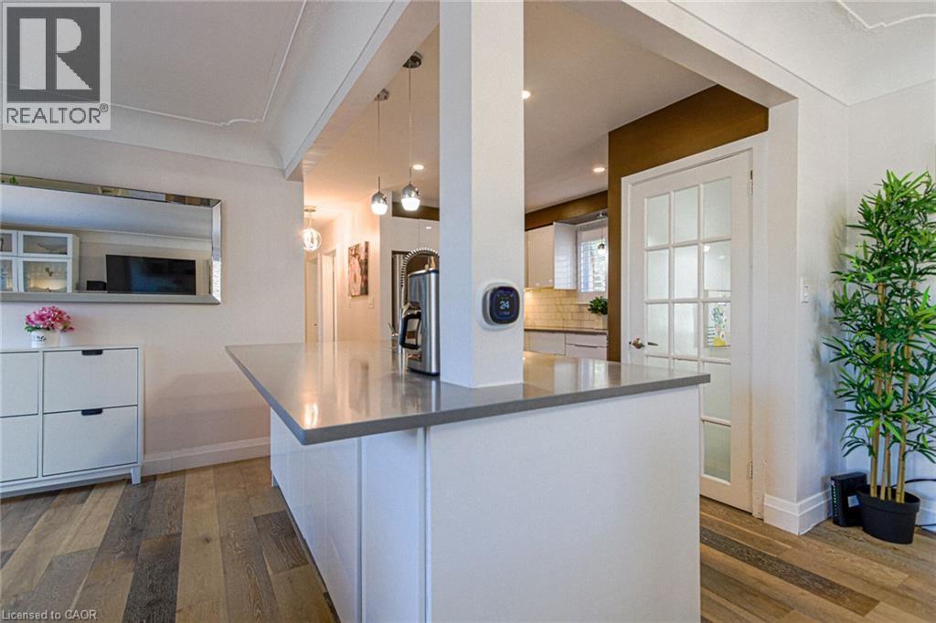 Wood-finish flooring, white paneled cabinetry, pendant lighting, built-in counter space, and a glass-paneled door - 2105 Maplewood Drive, Burlington, ON - Indoor Photo Showing Kitchen