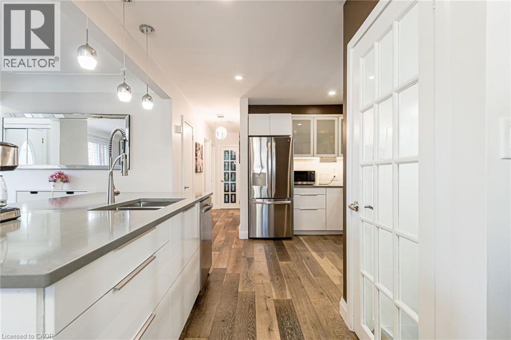Kitchen featuring a large island with an undermount sink, stainless steel appliances, white cabinetry, and wood-finish flooring - 2105 Maplewood Drive, Burlington, ON - Indoor Photo Showing Kitchen With Stainless Steel Kitchen With Double Sink With Upgraded Kitchen