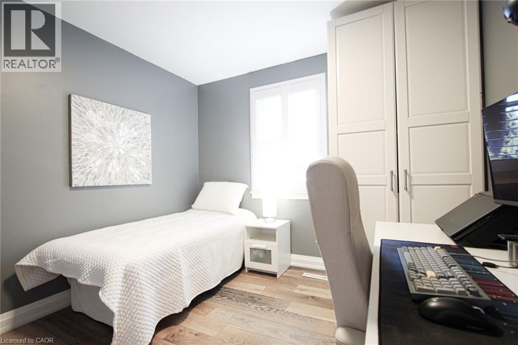 Wood-finish flooring, light gray wall color, built-in white cabinetry with metal pulls, and a window with white trim - 2105 Maplewood Drive, Burlington, ON - Indoor Photo Showing Bedroom