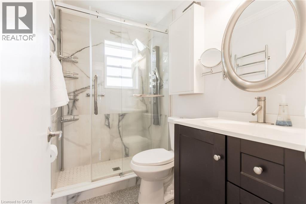 Glass-enclosed shower with white marble-style wall panels, hexagonal tile flooring, and a window - 2105 Maplewood Drive, Burlington, ON - Indoor Photo Showing Bathroom