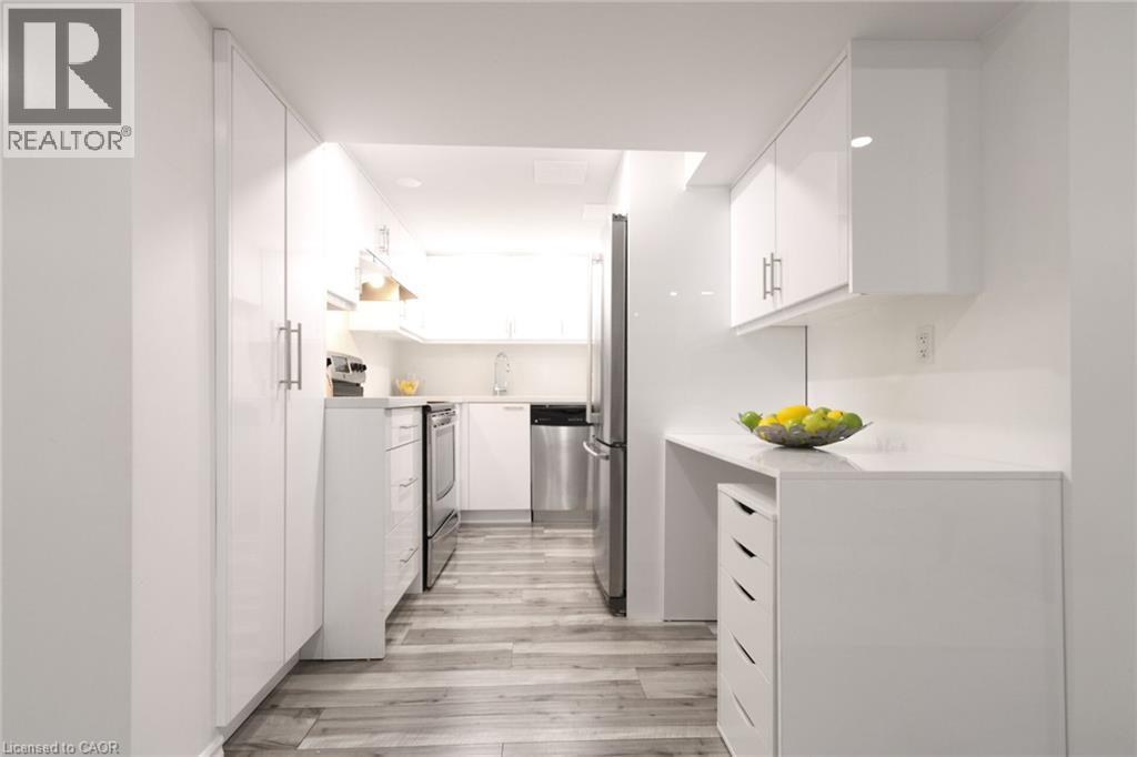 Galley kitchen featuring white cabinetry, stainless steel appliances, light-toned wood-finish flooring, and recessed lighting - 2105 Maplewood Drive, Burlington, ON - Indoor