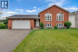Brick exterior featuring a two-car garage, arched upper windows with white shutters, and a well-maintained front lawn - 