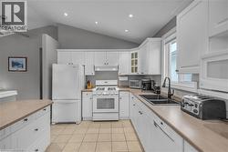 Kitchen featuring white cabinetry, a dual basin sink with a matte black faucet, tile flooring, an angled ceiling, and recessed lighting - 