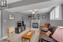 Carpeted living space featuring a white mantel fireplace, built-in shelving, and a ceiling fan - 