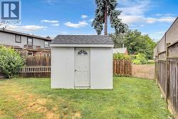 Backyard featuring a white storage shed with an arched glass insert door, a dark shingle roof, and surrounding wood fencing - 