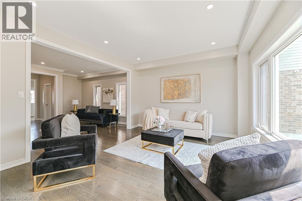 Sophisticated open-concept living space featuring recessed ceiling lighting, large windows with natural light, wood-finish flooring throughout, and a black leather accent chair with brass-finished fra - 24 Weatherall Avenue, Cambridge, ON - Indoor Photo Showing Living Room