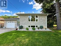 Brick exterior with white trim, attached single-car garage, manicured front lawn, and mature trees - 