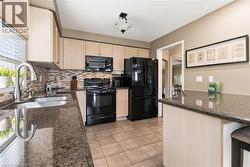 Spacious kitchen featuring light wood cabinetry, granite countertops, mosaic tile backsplash, black stainless steel appliances, and tile flooring throughout - 