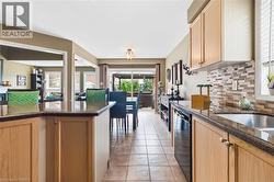 Kitchen featuring wood cabinetry, granite countertops, a stainless steel sink, and a multi-tone tile backsplash - 