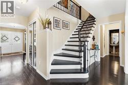 Dark wood-finish flooring throughout, a grand staircase with dark treads and balusters, double entry doors with decorative glass inserts, and a built-in mirrored closet - 