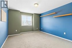 Versatile bedroom featuring dual-tone wall finishes in soft sage and vibrant blue, natural light from a generous window, recessed ceiling lighting, and built-in wooden shelving - 