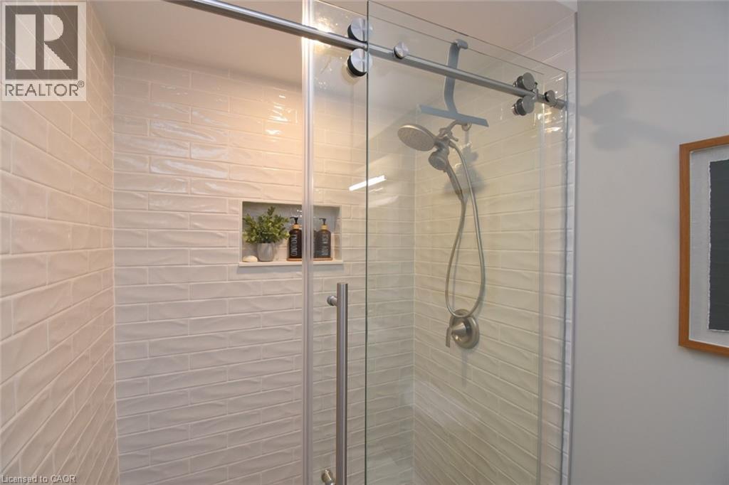 Tiled shower stall with a built-in niche, glass sliding door, and brushed nickel fixtures - 470 Amanda Crescent, Burlington, ON - Indoor Photo Showing Bathroom