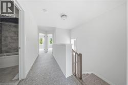 Carpeted hallway with a white balustrade and staircase, leading to a bathroom featuring a white tub and tiled surround - 