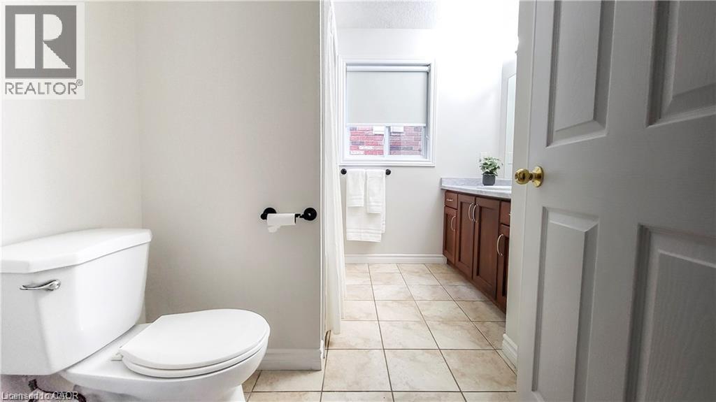 Ceramic tile flooring with a wood-finish vanity and white countertop - 128 Udvari Crescent Unit# A, Kitchener, ON - Indoor Photo Showing Bathroom
