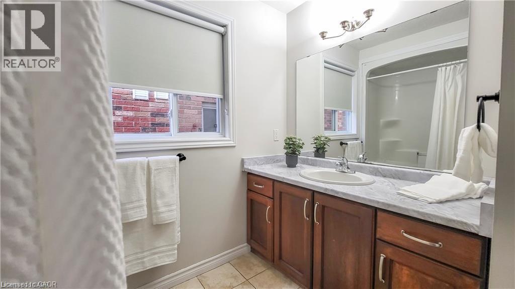 Bathroom featuring a single vanity with wood-finish cabinetry, a large mirror, and a bathtub with shower - 128 Udvari Crescent Unit# A, Kitchener, ON - Indoor Photo Showing Bathroom