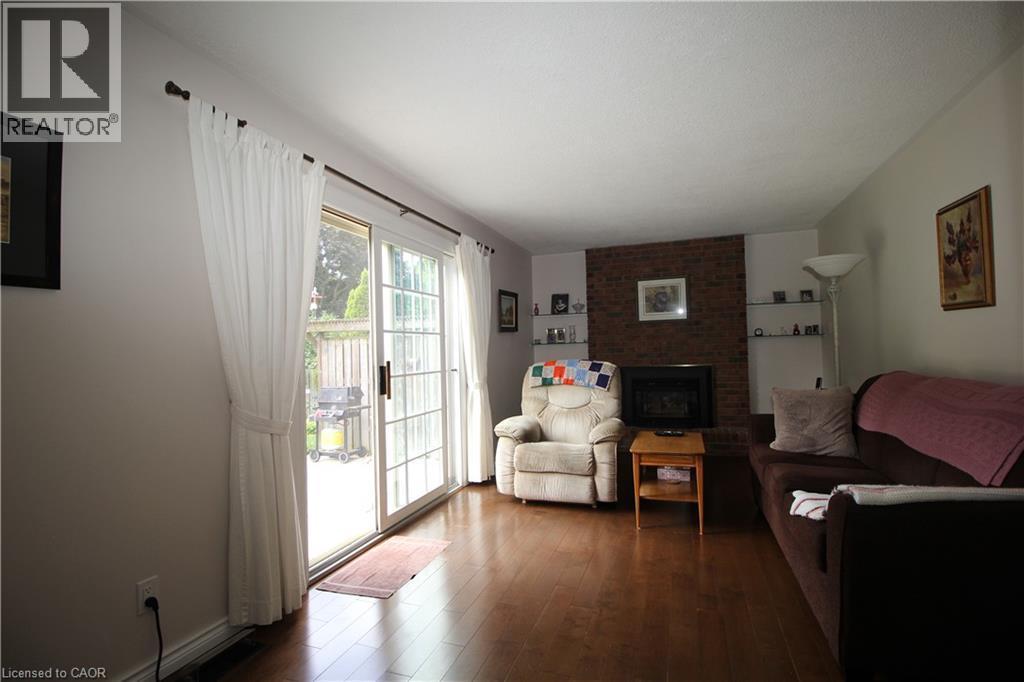 Expansive wood-finish flooring, brick accent wall with fireplace, built-in shelving, and sliding glass door leading to an outdoor patio - 14 Berkley Crescent, Simcoe, ON - Indoor Photo Showing Living Room With Fireplace