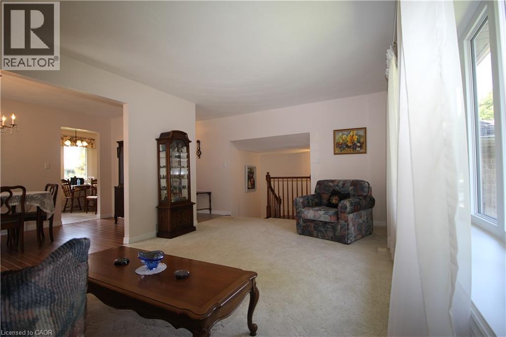 Carpeted living area with a large window, offering a wide opening to a dining space with wood-finish flooring - 14 Berkley Crescent, Simcoe, ON - Indoor Photo Showing Living Room