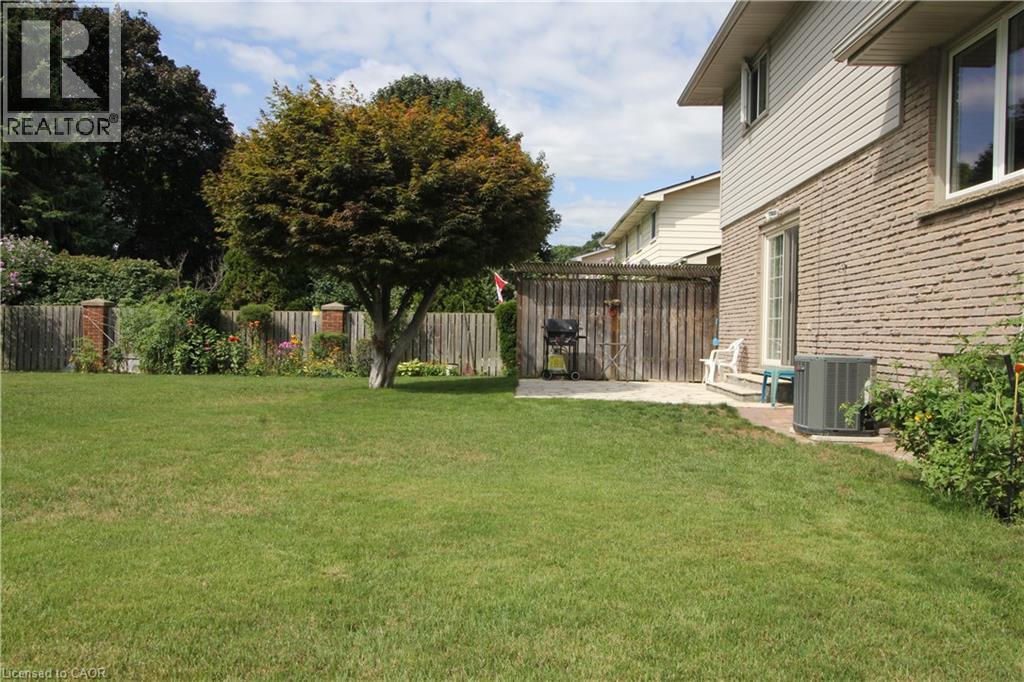 Expansive green space featuring a paved patio area, mature trees, and a wooden fence with brick posts - 14 Berkley Crescent, Simcoe, ON - Outdoor