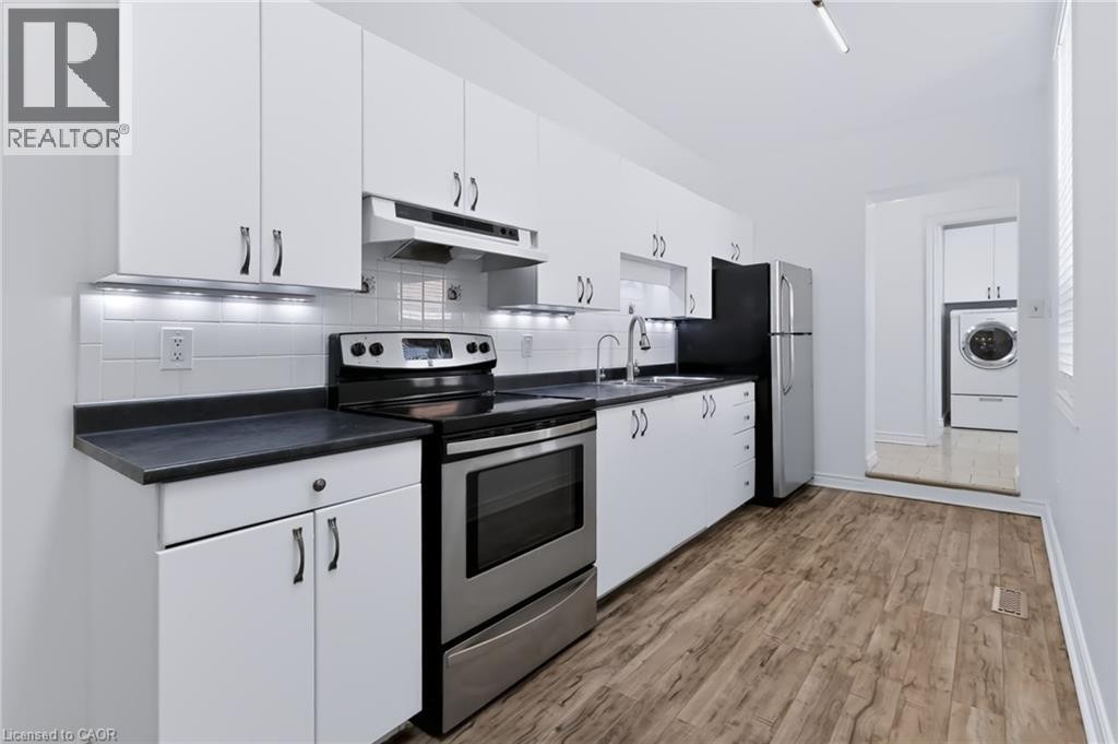White cabinetry with dark hardware, dark countertops, a stainless steel range, and wood-finish flooring - 442 King William Street, Hamilton, ON - Indoor Photo Showing Kitchen