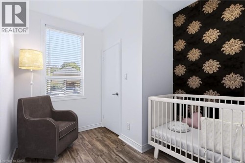 Wood-finish flooring, single window with blinds, white trim, solid interior door, and a decorative accent wall - 442 King William Street, Hamilton, ON - Indoor Photo Showing Bedroom