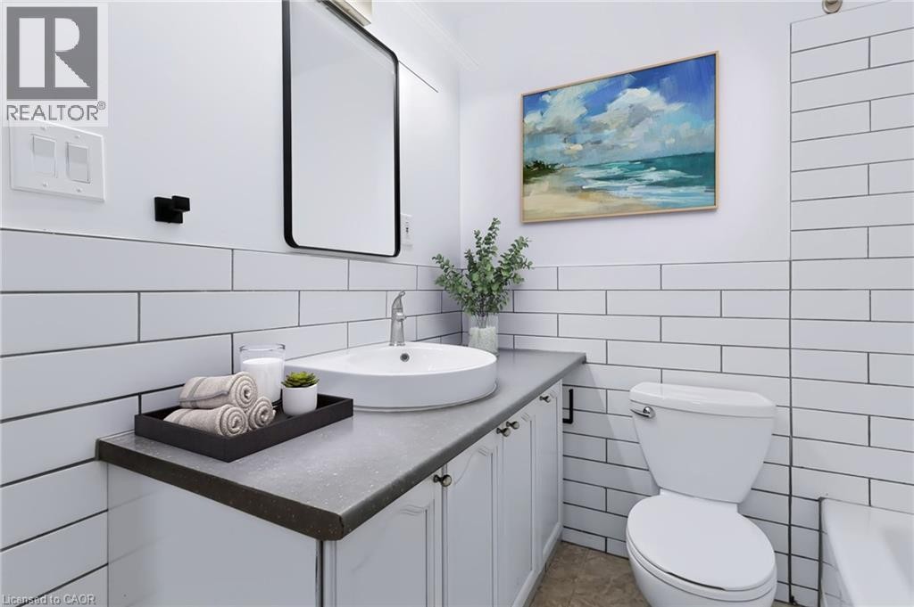 White subway tile wainscoting, a solid surface vanity top, and a white vessel sink with a chrome faucet - 442 King William Street, Hamilton, ON - Indoor Photo Showing Bathroom
