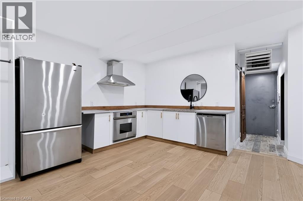 Kitchen featuring wood-finish flooring, white cabinetry with gold-tone hardware, stainless steel appliances, and L-shaped countertops - 442 King William Street, Hamilton, ON - Indoor Photo Showing Kitchen