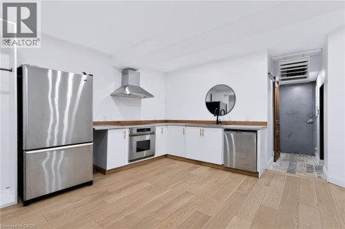 Kitchen featuring wood-finish flooring, white cabinetry with gold-tone hardware, stainless steel appliances, and L-shaped countertops - 442 King William Street, Hamilton, ON - Indoor Photo Showing Kitchen