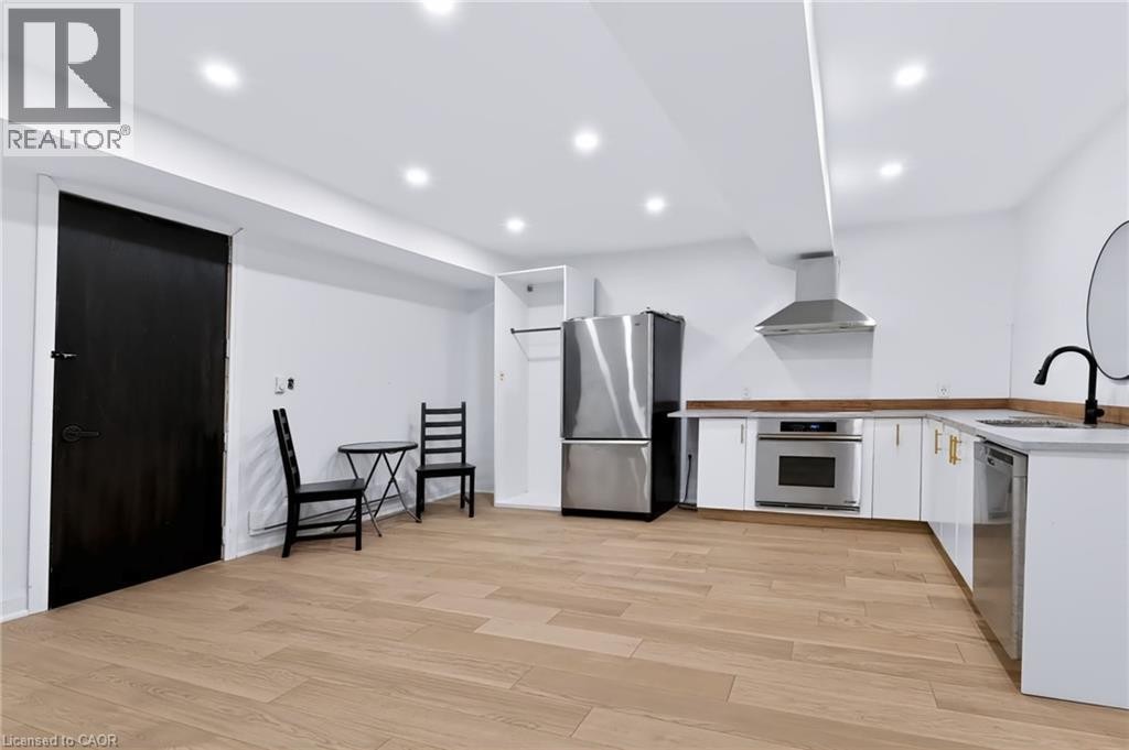 Wood-finish flooring, recessed lighting, stainless steel appliances, white cabinetry with gold-tone hardware, and a matte black gooseneck faucet - 442 King William Street, Hamilton, ON - Indoor Photo Showing Kitchen