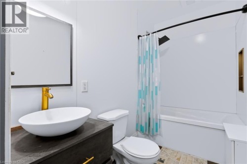 White bathroom with a rectangular vanity mirror, gold-finish faucet, and vessel sink - 442 King William Street, Hamilton, ON - Indoor Photo Showing Bathroom