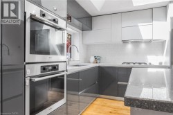 Sleek kitchen featuring dual-tone cabinetry, integrated stainless steel double ovens, a gas range with range hood, and light-colored countertops - 