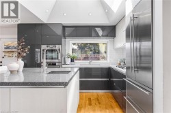 Sleek kitchen featuring gray high-gloss cabinetry, a spacious island with a built-in sink, stainless steel appliances, and wood-finish flooring - 