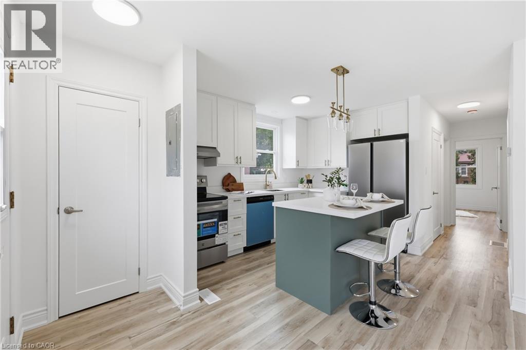 Open-concept kitchen featuring an island with a breakfast bar, stainless steel appliances, white cabinetry, and wood-finish flooring - 156 East 36Th Street, Hamilton, ON - Indoor Photo Showing Kitchen With Upgraded Kitchen