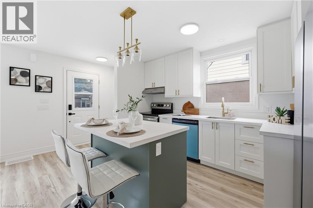 White cabinetry, gold-finish hardware, light wood-finish flooring, central island with seating, and a gold-finish chandelier - 156 East 36Th Street, Hamilton, ON - Indoor