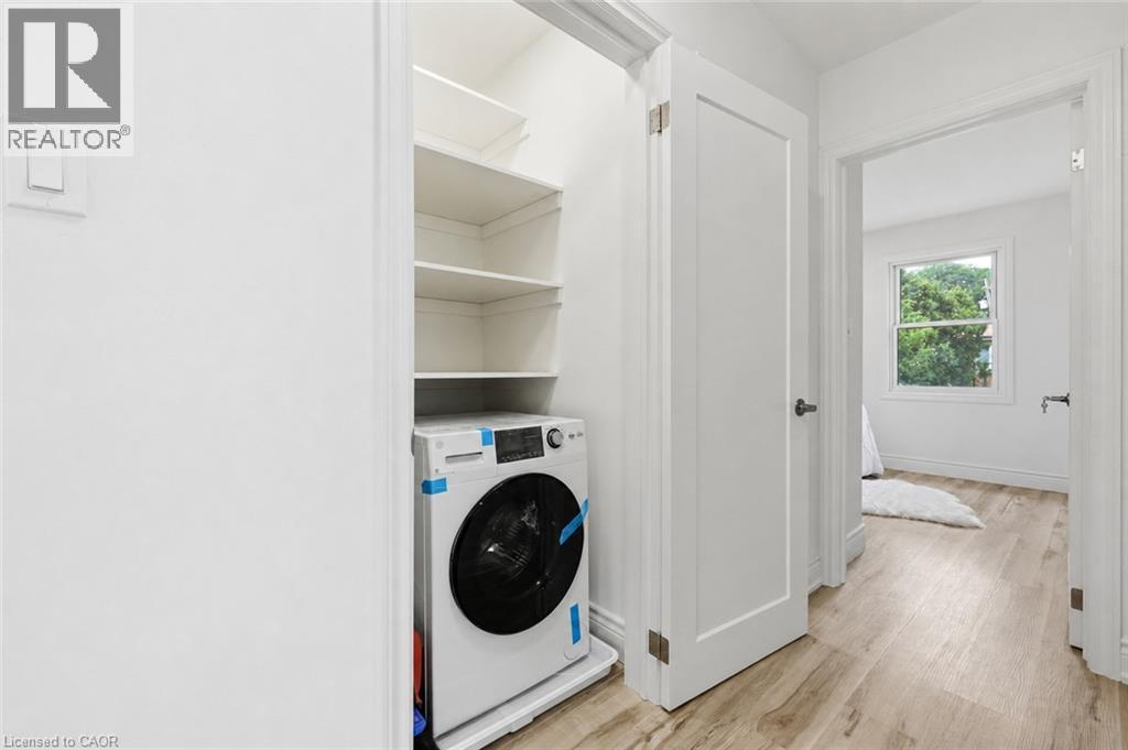 White front-load washer, built-in shelving, white paneled interior doors, and wood-finish flooring - 156 East 36Th Street, Hamilton, ON - Indoor Photo Showing Laundry Room