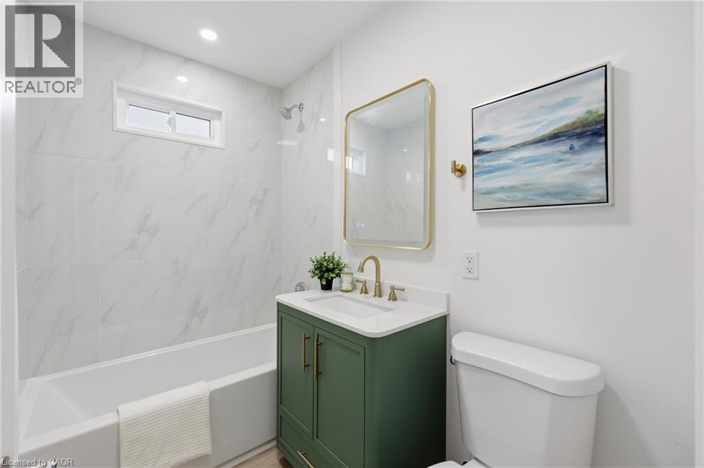 Full bathroom featuring a windowed shower-over-tub with large format wall tiling, a green vanity with brass hardware, and a framed mirror - 156 East 36Th Street, Hamilton, ON - Indoor Photo Showing Bathroom