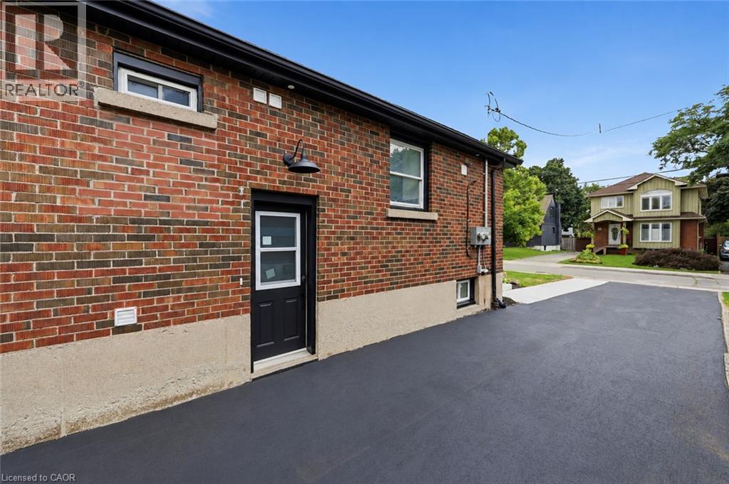 Brick exterior with a dark-finished entry door, exterior light fixture, and paved driveway - 156 East 36Th Street, Hamilton, ON - Outdoor