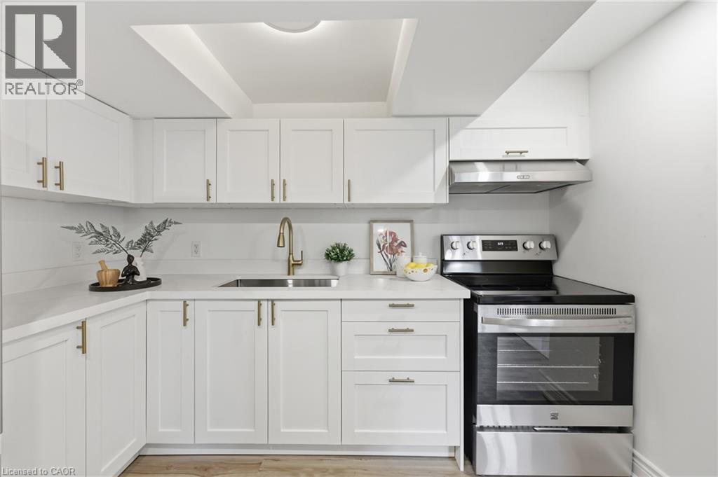White shaker-style cabinetry, stainless steel appliances, light-toned countertops, wood-finish flooring, and a gold-tone faucet - 156 East 36Th Street, Hamilton, ON - Indoor Photo Showing Kitchen With Upgraded Kitchen